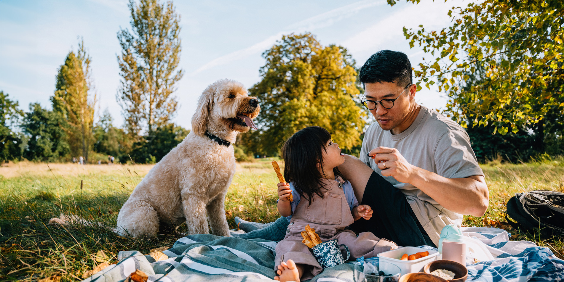 cheerful-young-asian-father-and-daughter-enjoying-picnic-with-their-dog-in-nature